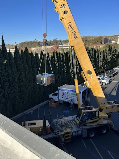 Comfort Air Conditioning & Heating crew crane-lifting a packaged HVAC unit above a San Diego rooftop, branded box truck below