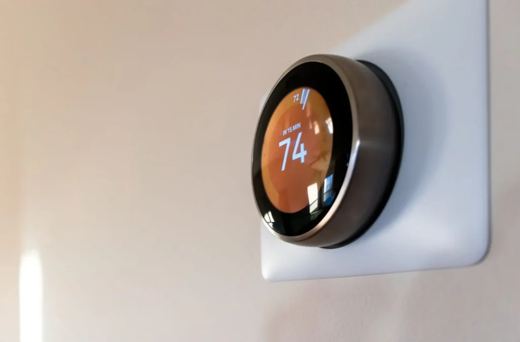 A modern thermostat displaying 74 degrees on a household wall.